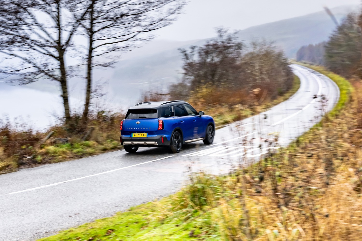 Three MINI models racing. A MINI Cooper, Countryman and Convertible captured from the side, speeding down an open road.